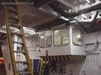 The car-deck main control cabin. This photo is looking toward the forward starboard side of the car deck. The yellow cockpit access ladder is visible, as is the open bow door. The ladder was initially intended to be a retractable feature, allowing crew access and then the sealing of the cockpit hatch (climbing the ladder leaves you at floor level upon entering head-first into the rear of the cockpit, so a bit of fearless gymnastics is required to get up into the flight deck!). It was however decided to bolt down and strengthen the ladder, making it a permanent fixture. This added extra strength to the roof, as well as a quick access route to the cockpit at any point during flight.